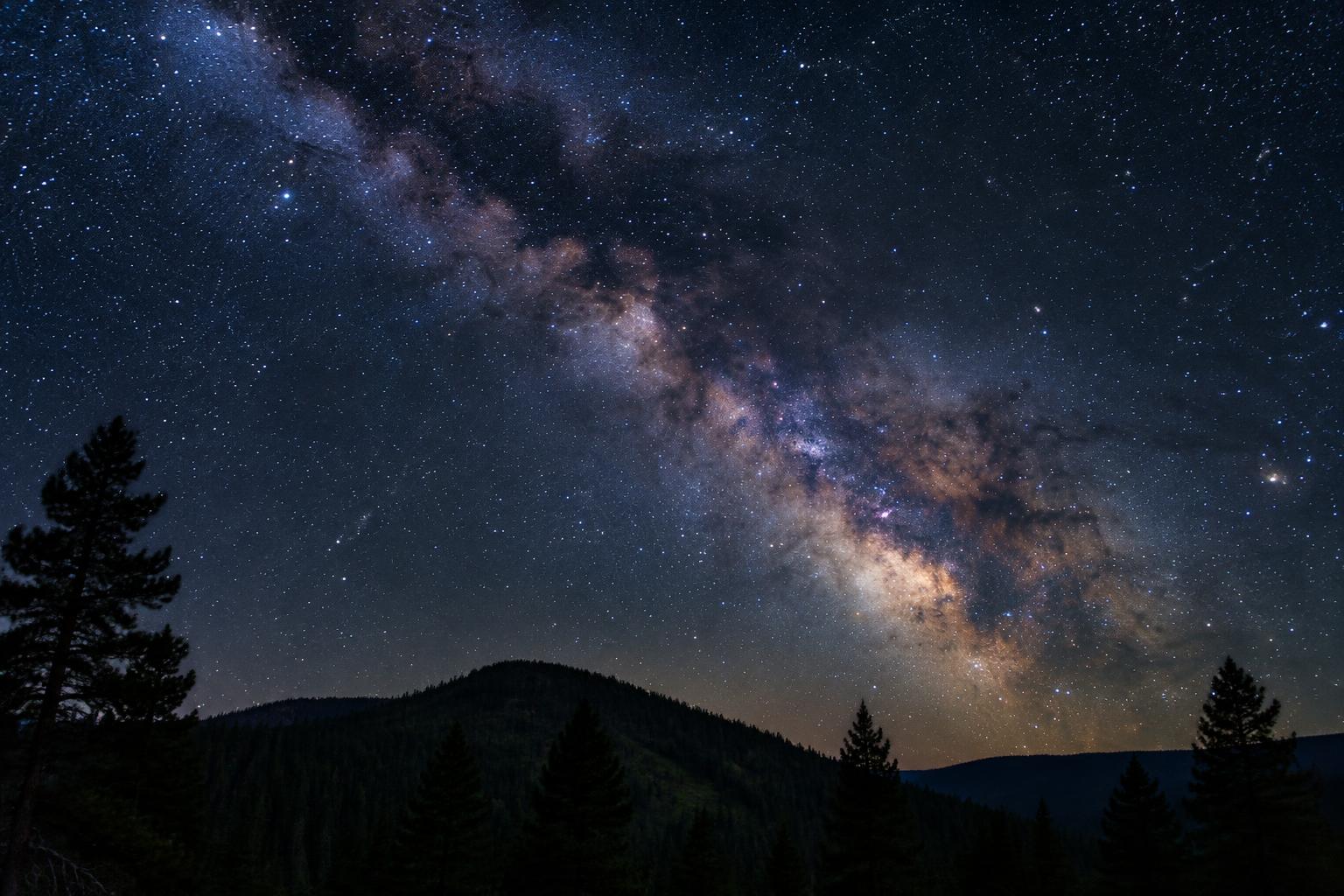 Star-filled night sky and the milky way above dark forested hills